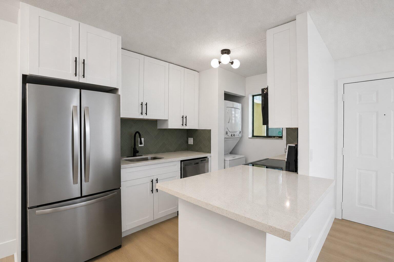 A modern kitchen features white cabinets, stainless steel appliances, a quartz island, and gray backsplash — 588 Trace Circle # 102, Deerfield Beach FL 33441, DEERFIELD BEACH, FL
