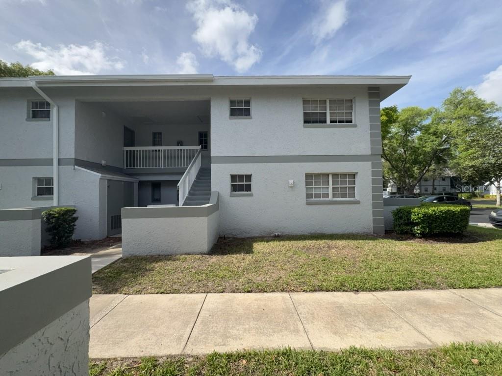 A two-story apartment building exterior with gray stucco walls and an open-air stairwell — 454 FAIRWAYS CIRCLE UNIT B204, OCALA, FL