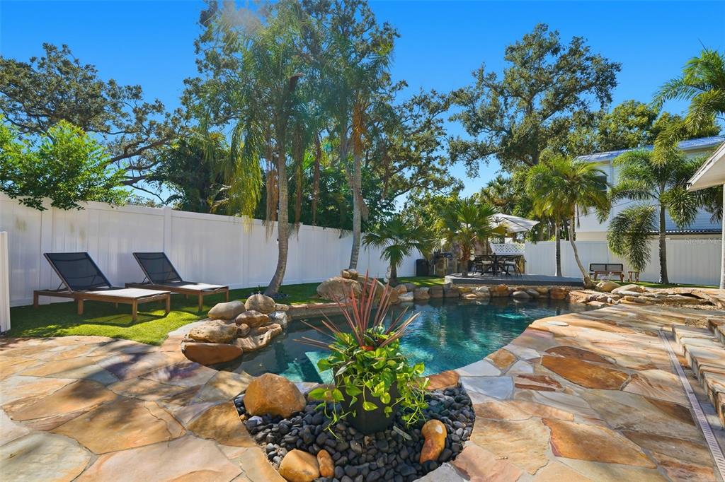 A backyard features a stone-paved pool deck, a swimming pool, lounge chairs, and palm trees — 517 AVERY AVENUE, CRYSTAL BEACH, FL