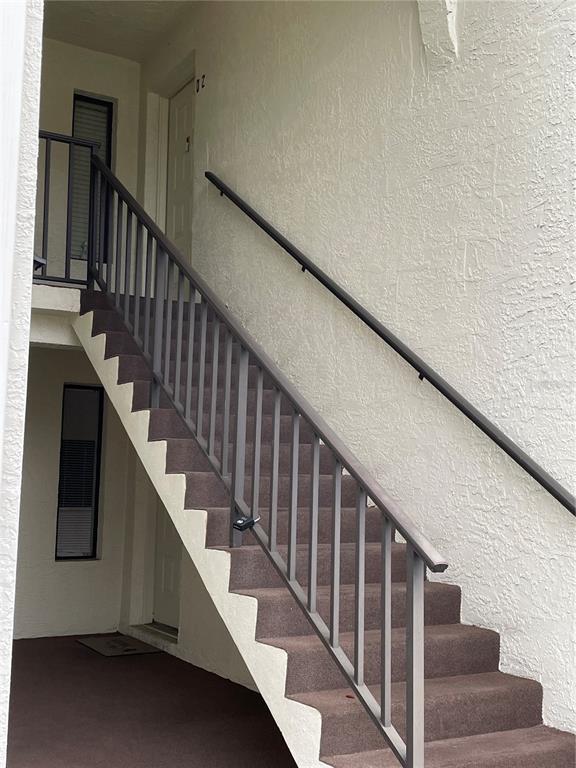 An exterior staircase with dark metal railings leads to an upper-level apartment entrance — 2688 PINE RIDGE WAY N UNIT D2, PALM HARBOR, FL