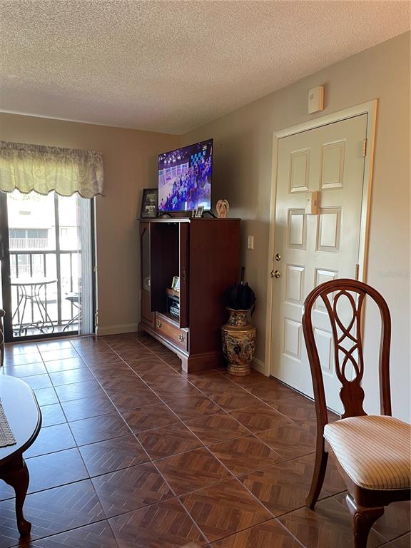 A living area features tile flooring, a wooden entertainment center, and a door to a balcony — 2688 PINE RIDGE WAY N UNIT D2, PALM HARBOR, FL