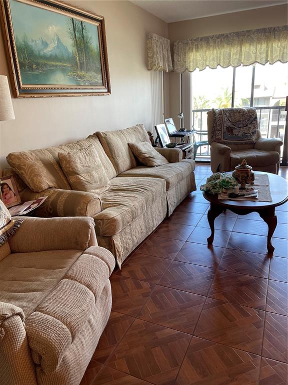 A living room features a beige sofa, matching armchair, coffee table, and a large landscape painting — 2688 PINE RIDGE WAY N UNIT D2, PALM HARBOR, FL