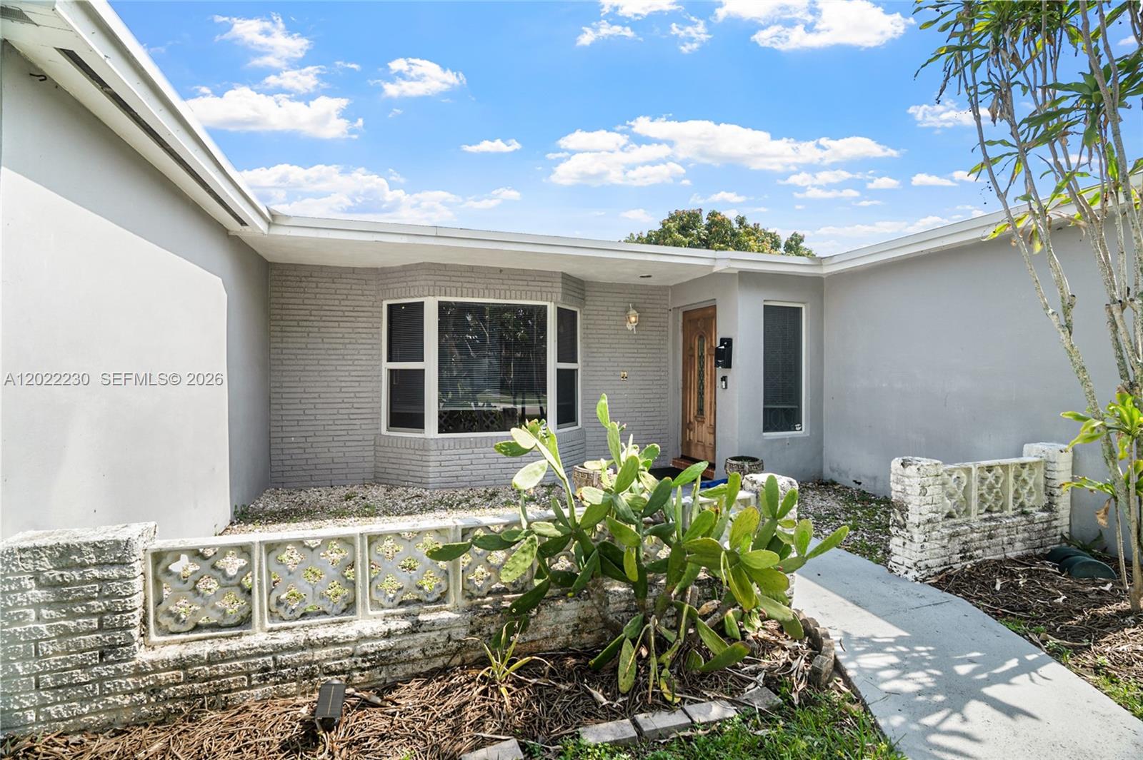 The exterior of a single-story house features a gray brick facade, a bay window, and a decorative concrete block wall — 6667 NW 1st St, Margate FL 33063, MARGATE, FL