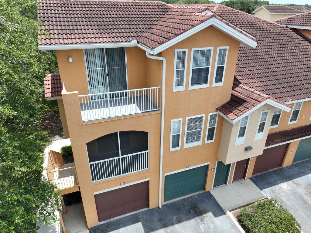 An aerial view of a multi-story orange stucco townhouse with a tile roof and garages — 12208 WILD IRIS WAY UNIT 110, ORLANDO, FL