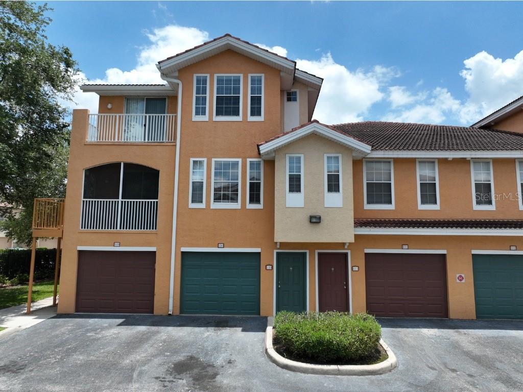 A three-story townhouse exterior with orange stucco, multiple garages, and a small front garden — 12208 WILD IRIS WAY UNIT 110, ORLANDO, FL