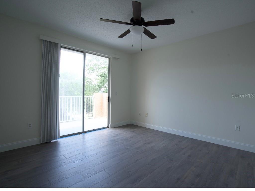 An empty bedroom features dark wood-look flooring, white walls, a ceiling fan, and sliding doors — 12208 WILD IRIS WAY UNIT 110, ORLANDO, FL