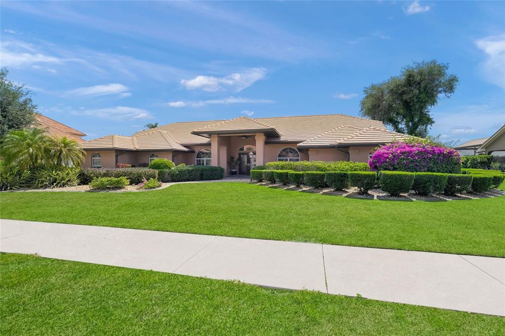 A single-story house with a tan stucco exterior, tile roof, and manicured landscaping — 8838 WILD DUNES DRIVE, SARASOTA, FL