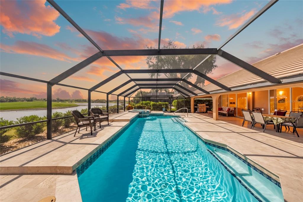 A rectangular swimming pool with a spa is enclosed by a screened lanai overlooking water — 8838 WILD DUNES DRIVE, SARASOTA, FL