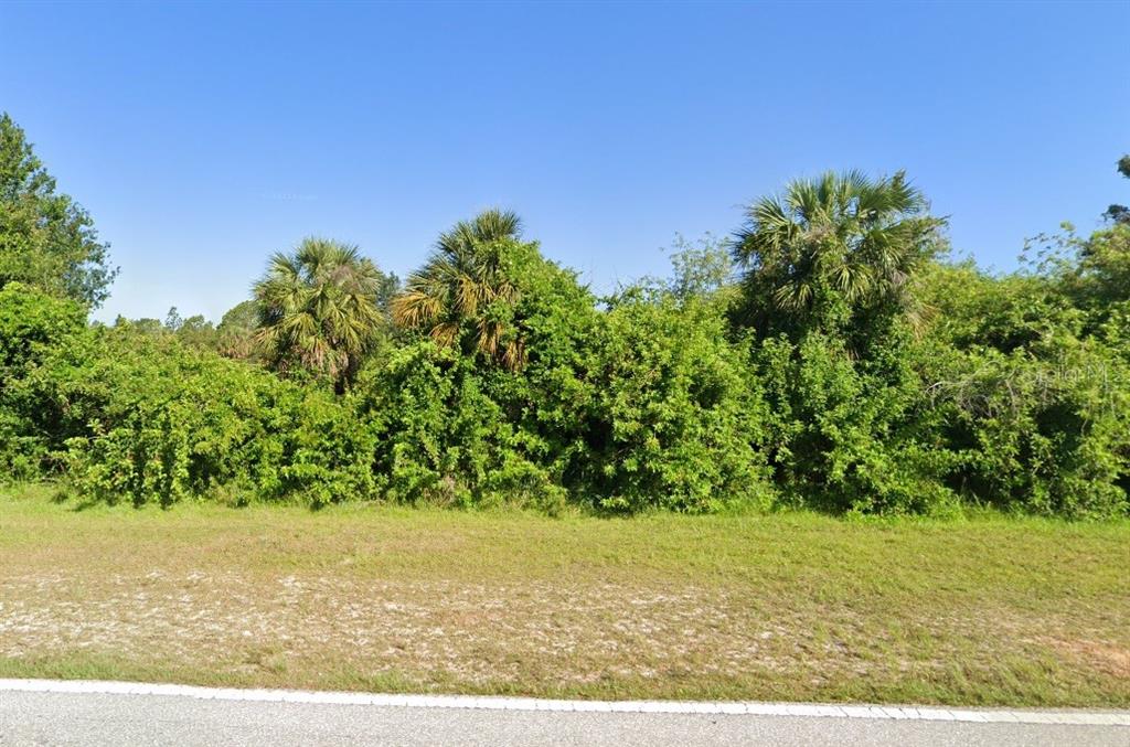 A grassy lot is bordered by dense green trees and palm trees under a clear sky — 15 PONCE DE LEON BOULEVARD, NORTH PORT, FL