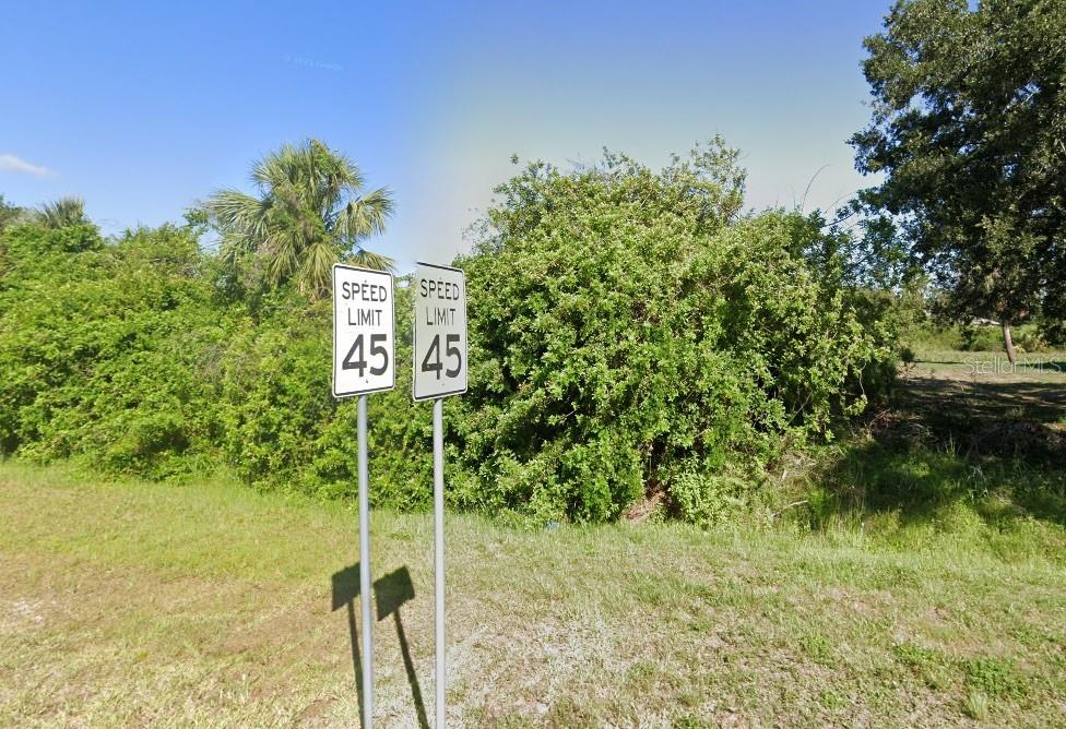 Two speed limit signs stand in a grassy area in front of dense green trees — 15 PONCE DE LEON BOULEVARD, NORTH PORT, FL