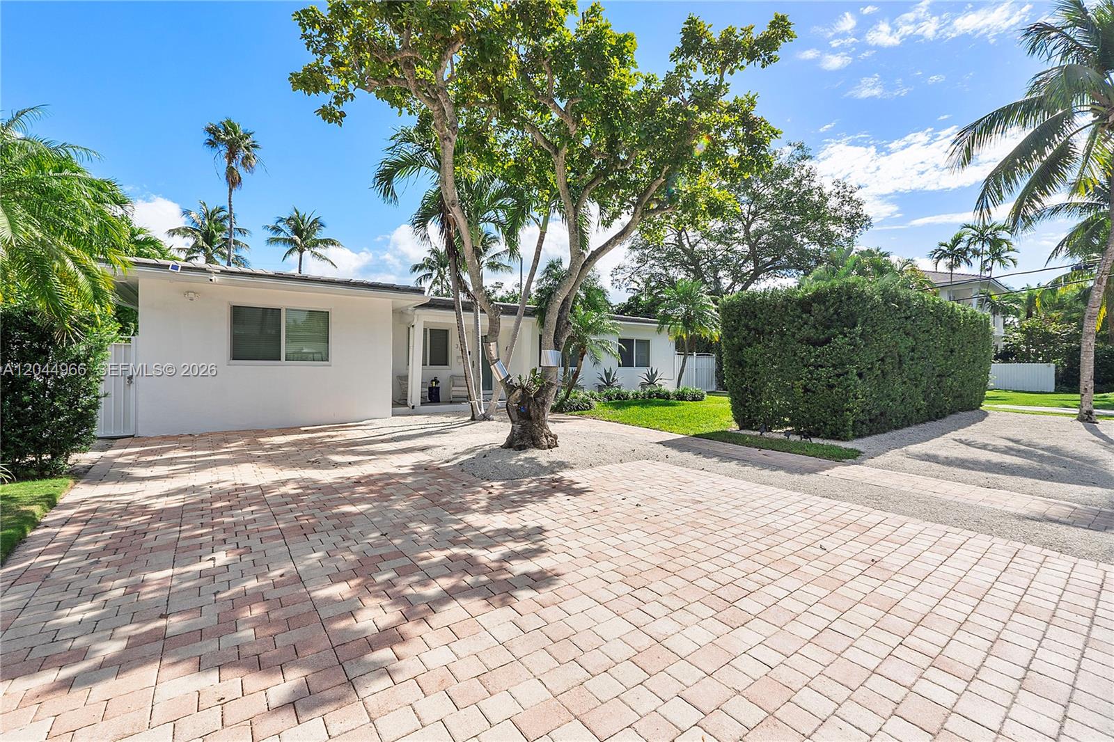 A white house features a paved driveway, a large tree, and a tall privacy hedge — 301 Hampton Ln, Key Biscayne FL 33149, KEY BISCAYNE, FL