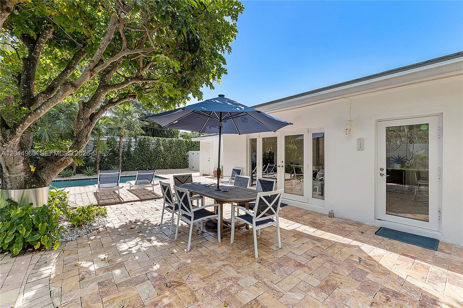 A patio features a dining set with a blue umbrella, lounge chairs, and a pool — 301 Hampton Ln, Key Biscayne FL 33149, KEY BISCAYNE, FL