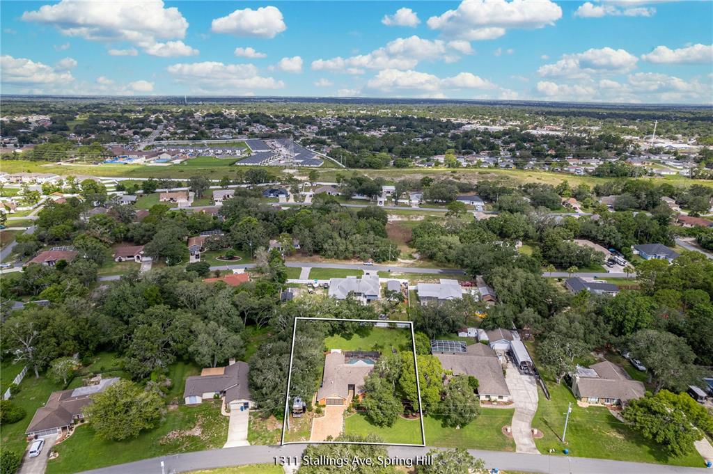 An aerial view shows a single-story house with a backyard pool surrounded by mature trees — 1311 STALLINGS AVENUE, SPRING HILL, FL