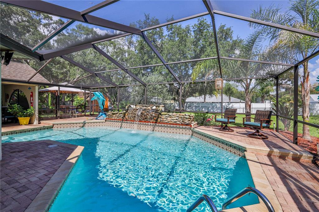 A screened-in swimming pool with a stone waterfall feature and a brick paver deck — 1311 STALLINGS AVENUE, SPRING HILL, FL