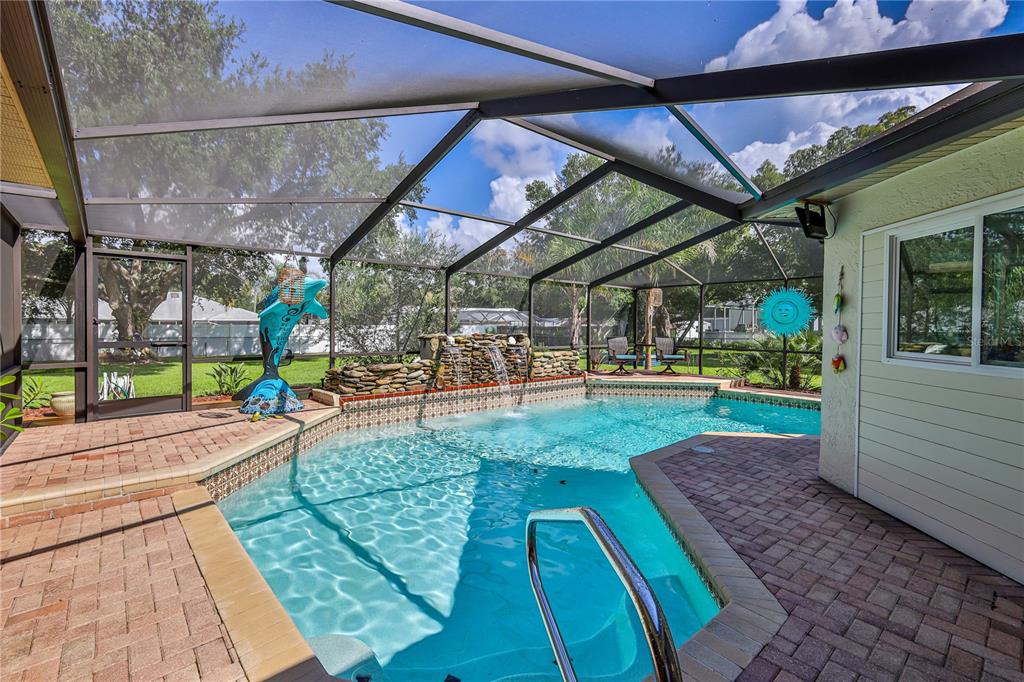A screened-in pool area features a stone waterfall, brick pavers, and a blue dolphin statue — 1311 STALLINGS AVENUE, SPRING HILL, FL
