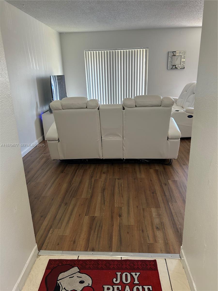 A living room features white reclining sofas on wood-look flooring facing a window with blinds — 17901 NW 68th Ave # R209, Hialeah FL 33015, HIALEAH, FL
