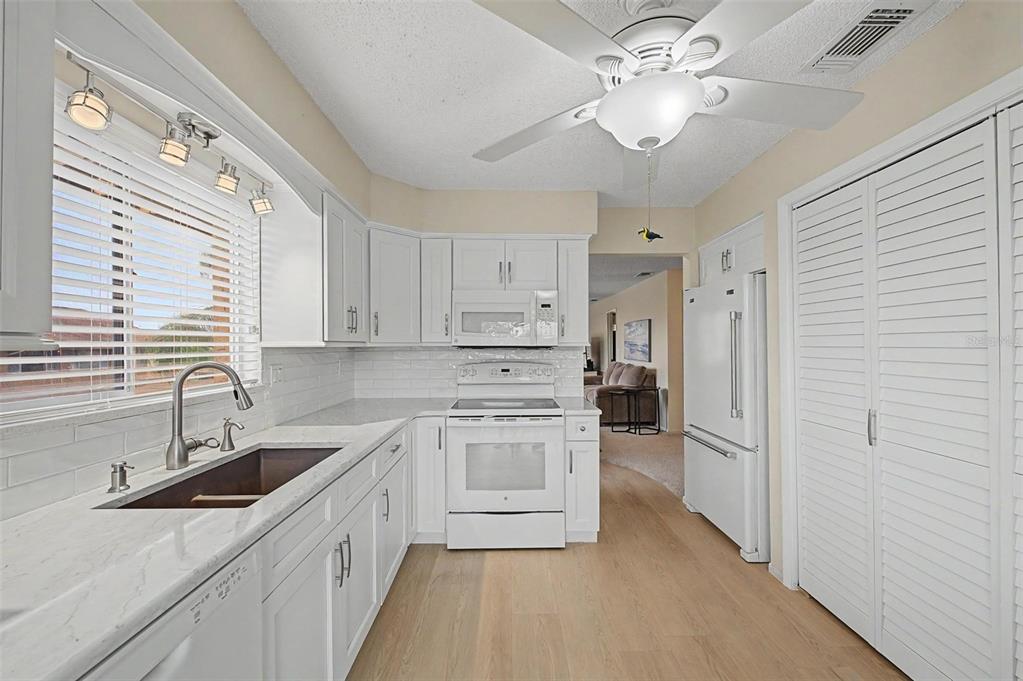 A white kitchen features light wood floors, white cabinetry, a subway tile backsplash, and appliances — 4009 LIGHTHOUSE WAY, NEW PORT RICHEY, FL