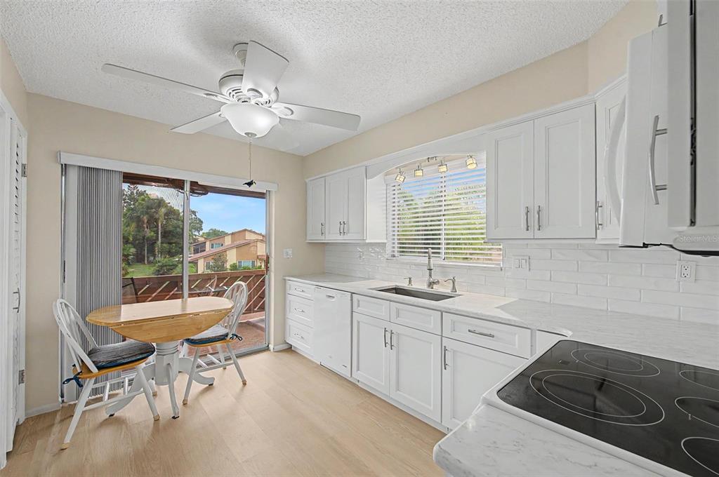 A kitchen with white cabinets, marble-look countertops, a ceiling fan, and a sliding glass door — 4009 LIGHTHOUSE WAY, NEW PORT RICHEY, FL