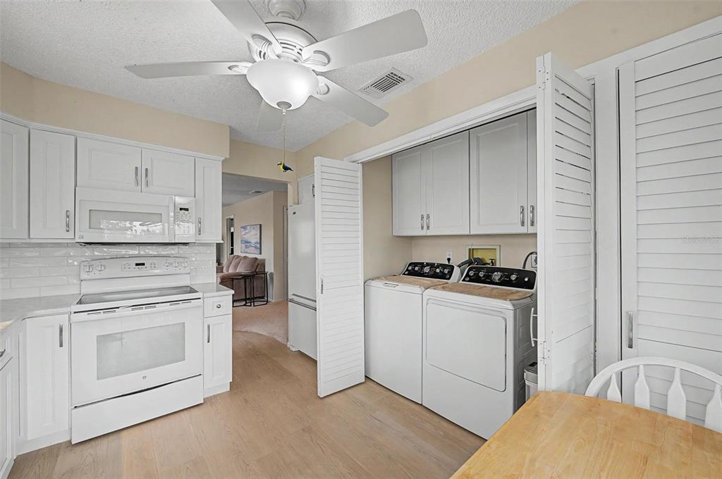 A kitchen features white cabinets, a white stove, and a laundry area with louvered doors — 4009 LIGHTHOUSE WAY, NEW PORT RICHEY, FL