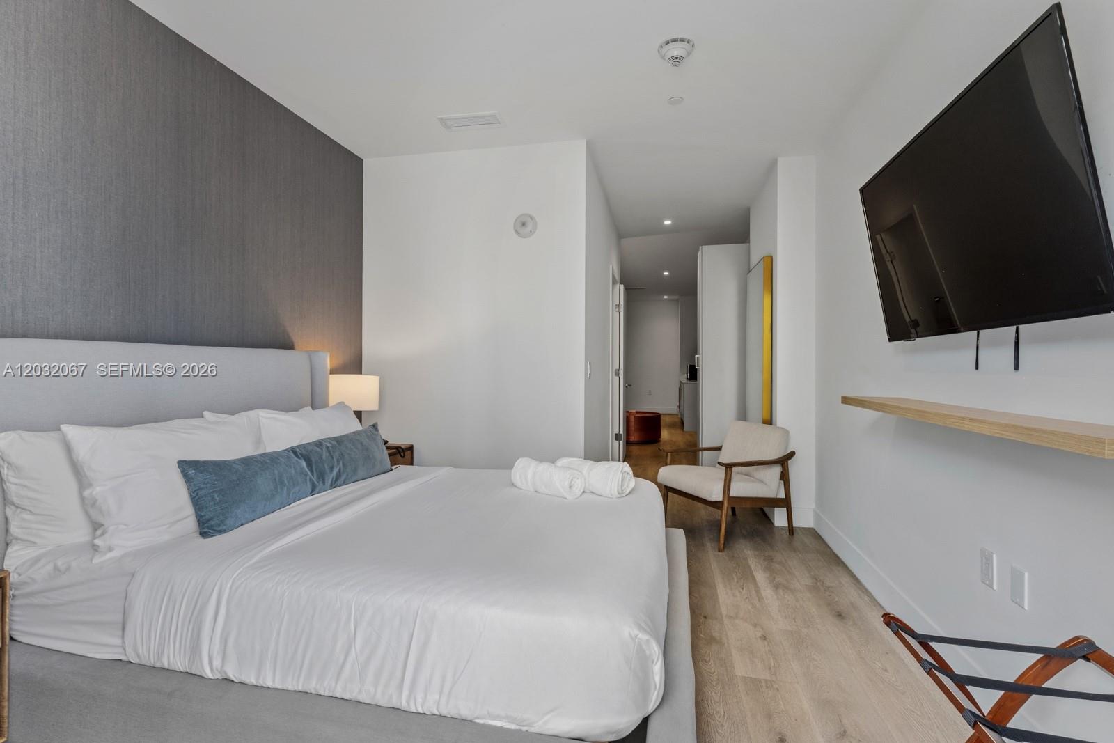 A bedroom features a gray upholstered bed, a wall-mounted television, and light wood flooring — 239 SW 9TH St # 301, Miami FL 33130, MIAMI, FL
