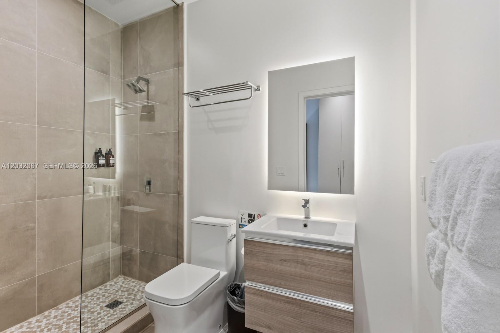 A modern bathroom features a glass-enclosed shower, a wood-toned vanity, and a backlit mirror — 239 SW 9TH St # 301, Miami FL 33130, MIAMI, FL