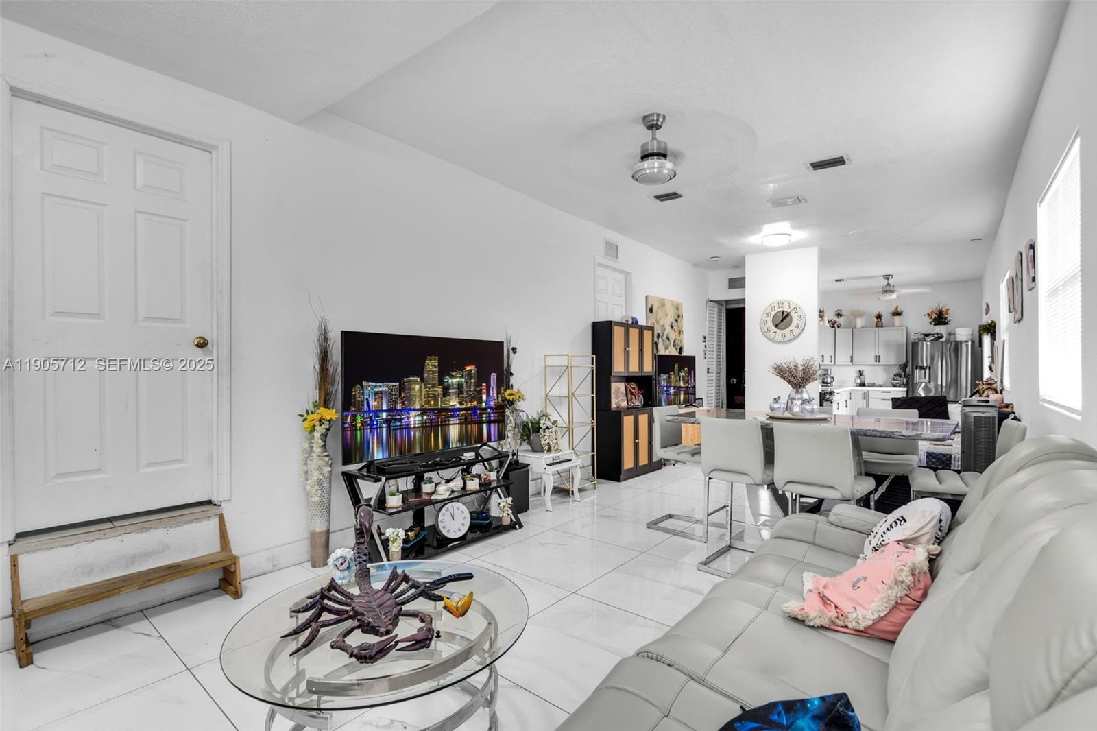 A living room with white tile floors, a grey sofa, and an open-concept kitchen — 3166 NW 102nd St, Miami FL 33147, MIAMI, FL