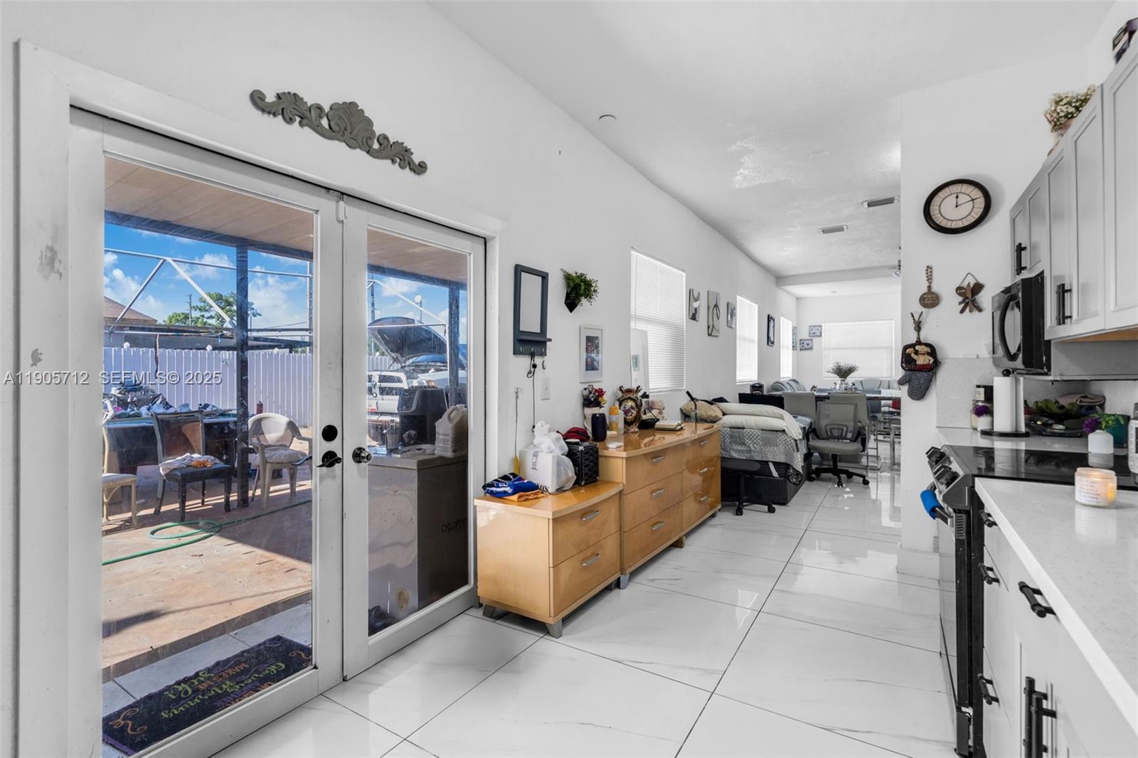 A kitchen and living area with white tile floors, a wooden dresser, and glass patio doors — 3166 NW 102nd St, Miami FL 33147, MIAMI, FL