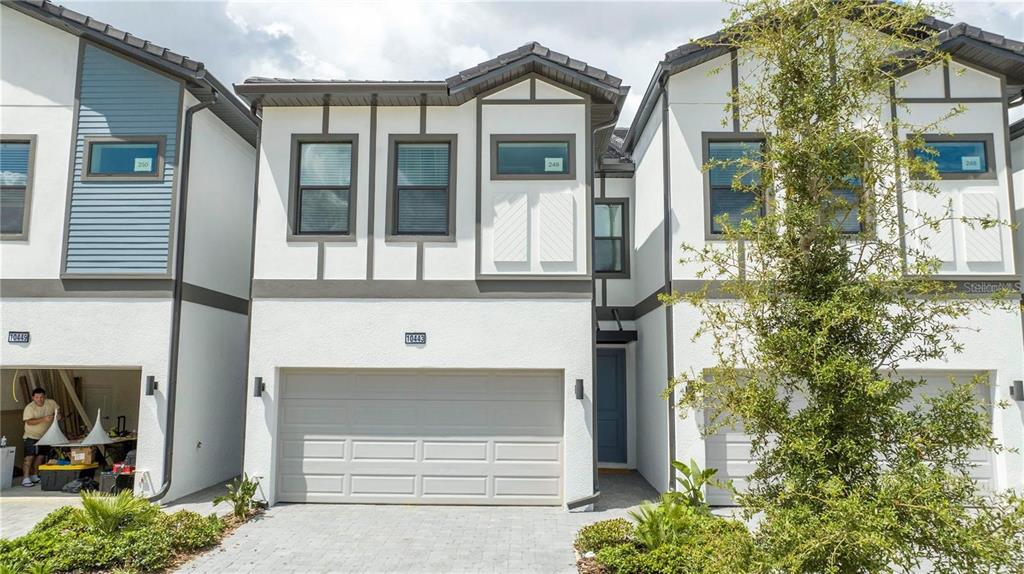 The exterior of a modern multi-story townhouse with a two-car garage and white stucco facade — 10443 EBB TIDE LANE, ORLANDO, FL
