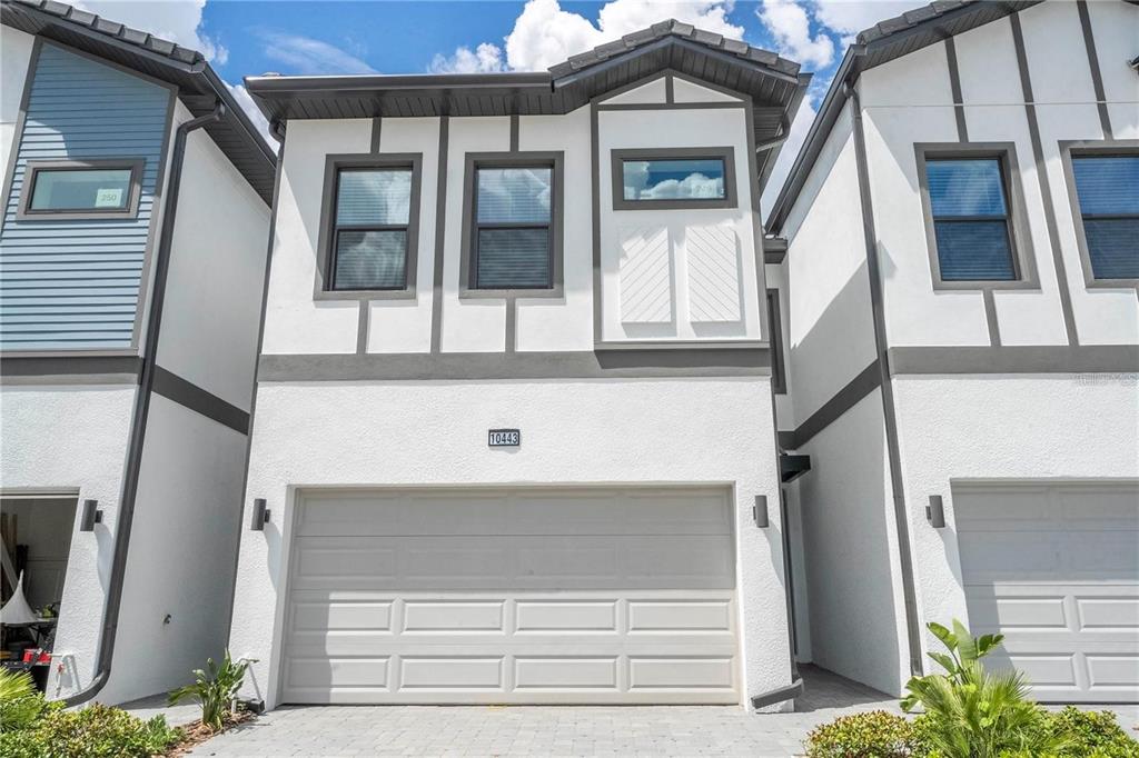 A two-story townhouse with a white stucco facade, dark trim, and a two-car garage — 10443 EBB TIDE LANE, ORLANDO, FL