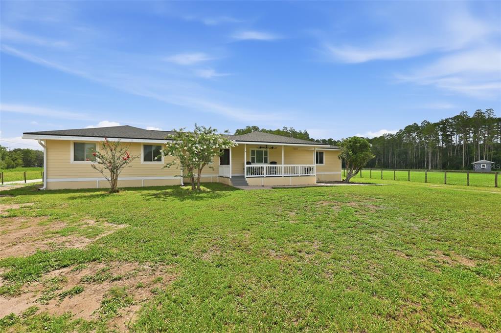 A yellow single-story house with a covered porch sits on a large grassy lot — 4700 TOWER ROAD, LAND O LAKES, FL