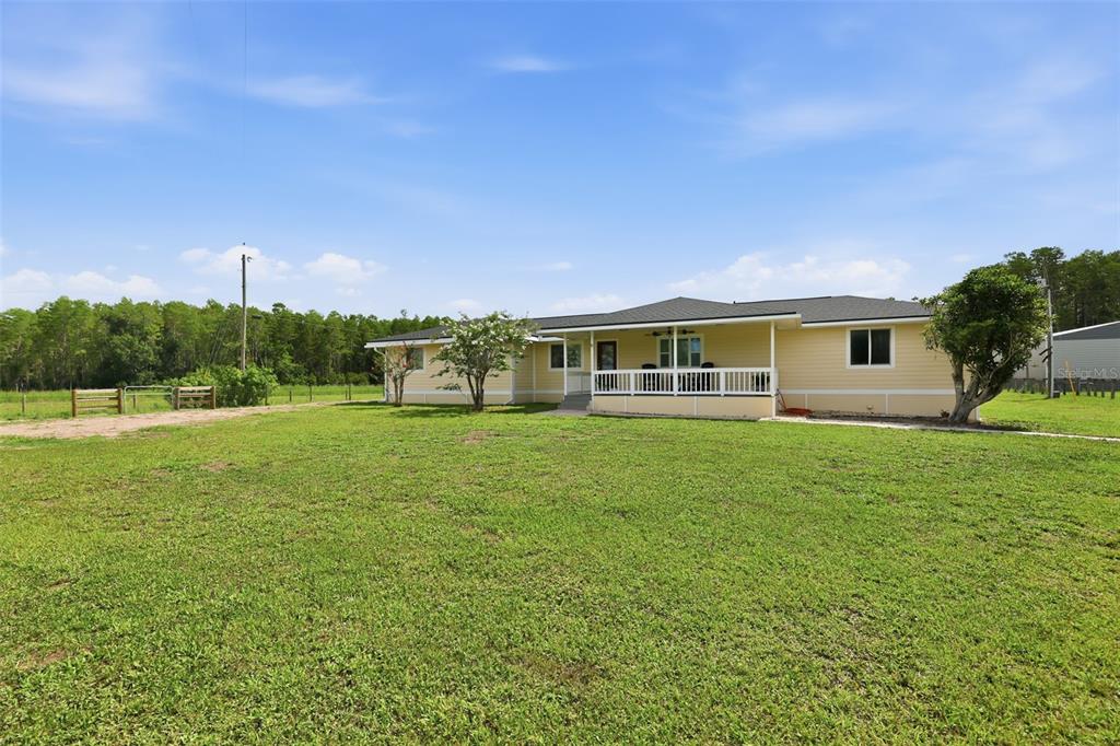 A yellow single-story house with a covered porch sits on a large grassy lot — 4700 TOWER ROAD, LAND O LAKES, FL