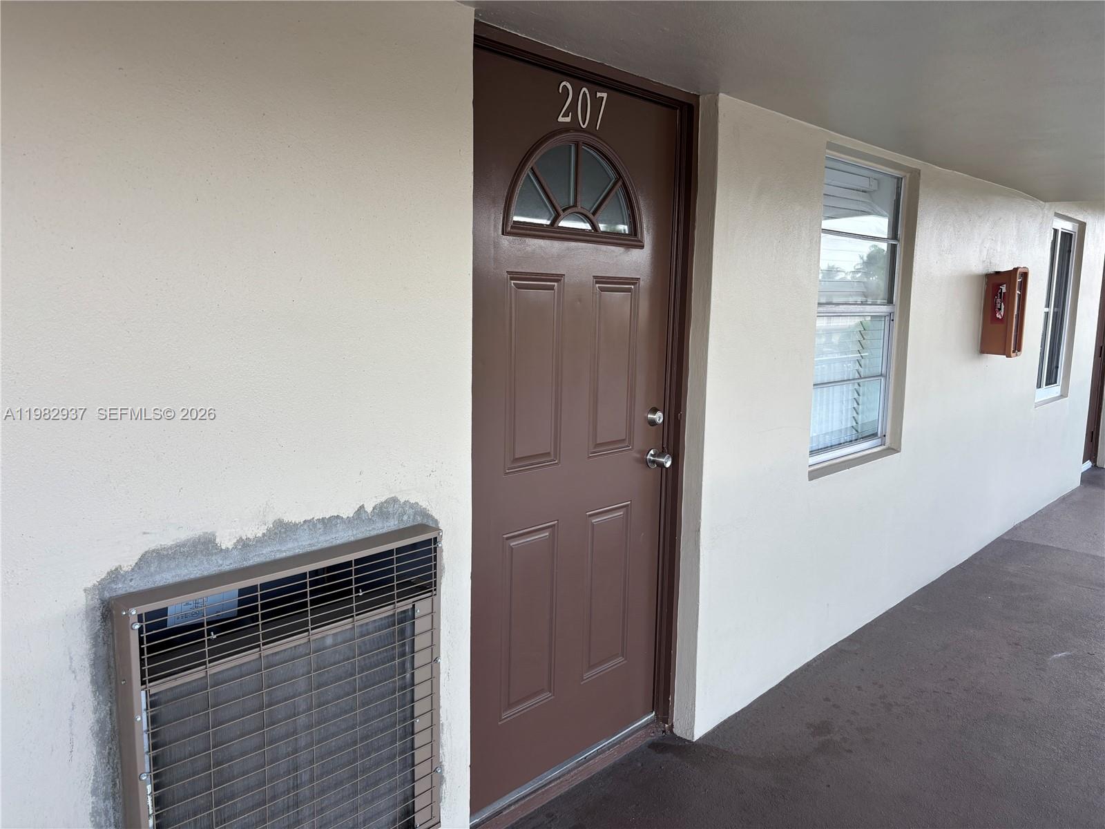 A brown door labeled 207 sits next to a window and an exterior air conditioning unit — 601 NW 80th Ave # 207, Margate FL 33063, MARGATE, FL