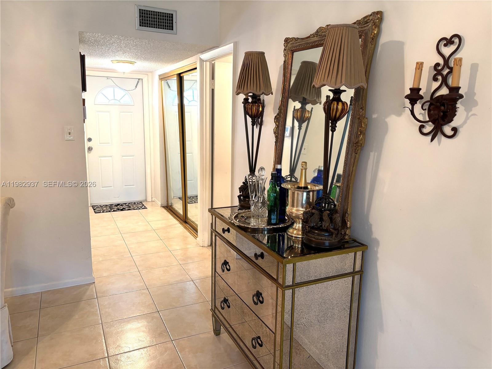 A mirrored chest with lamps and a mirror sits in a tiled entryway hallway — 601 NW 80th Ave # 207, Margate FL 33063, MARGATE, FL