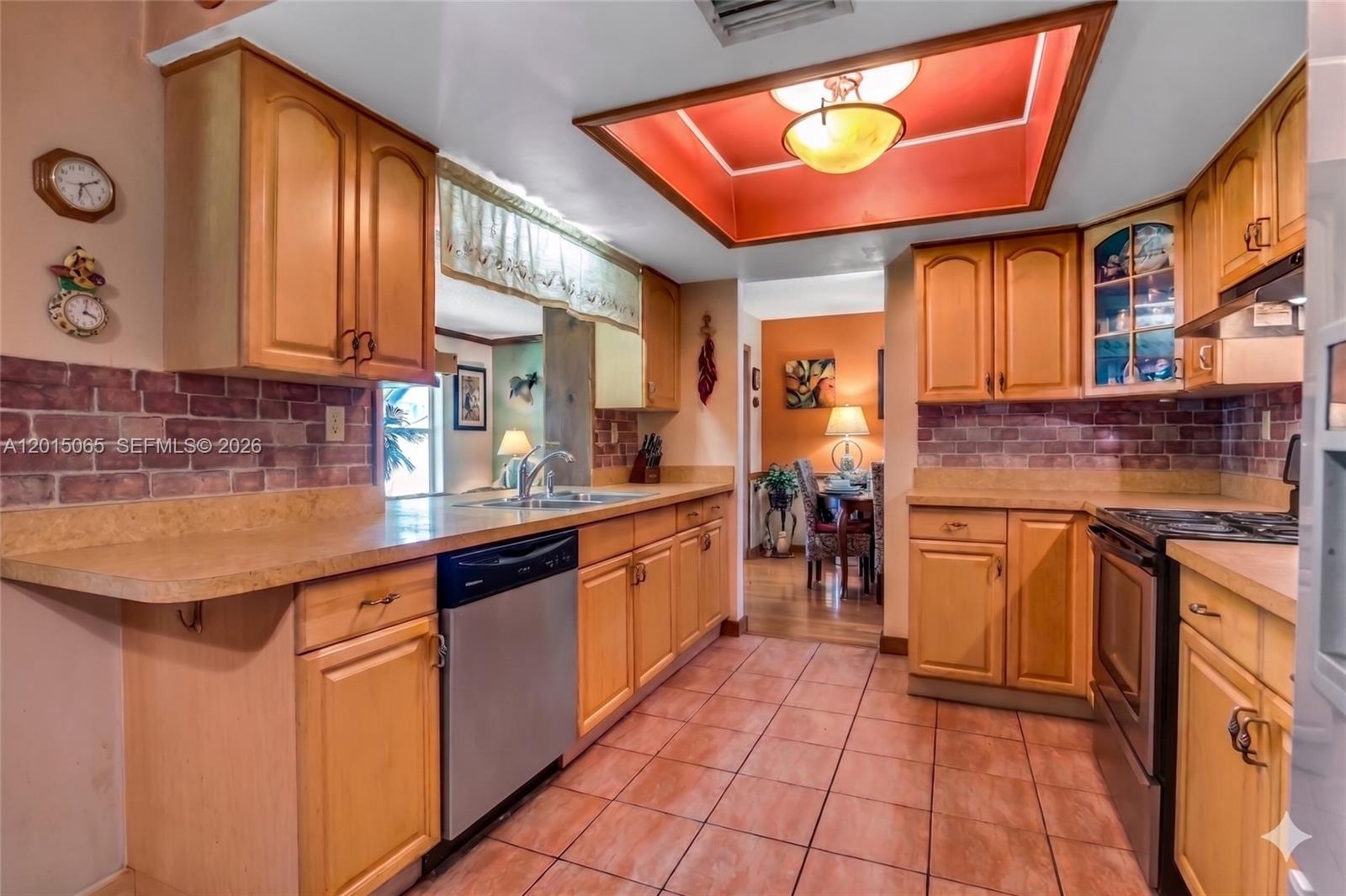 A kitchen features light wood cabinets, a brick backsplash, tile flooring, and a recessed ceiling — 4605 NW 47th Ct, Tamarac FL 33319, TAMARAC, FL