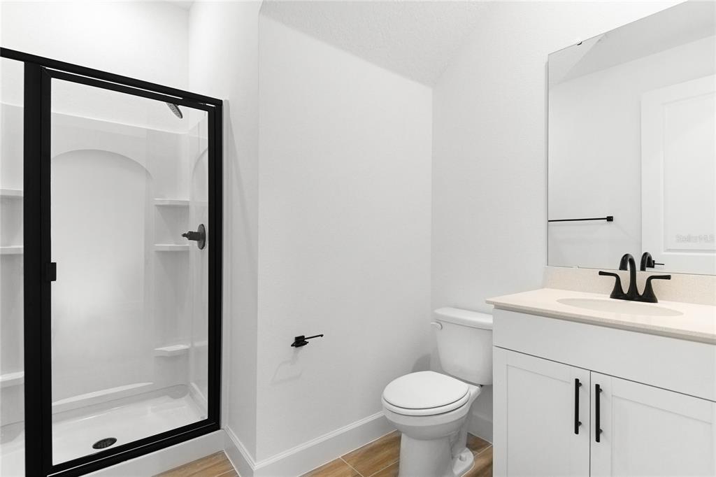 A bathroom features a glass-enclosed shower, a white vanity with a black faucet, and toilet — 740 WEKIVA RIDGE DRIVE, MOUNT DORA, FL