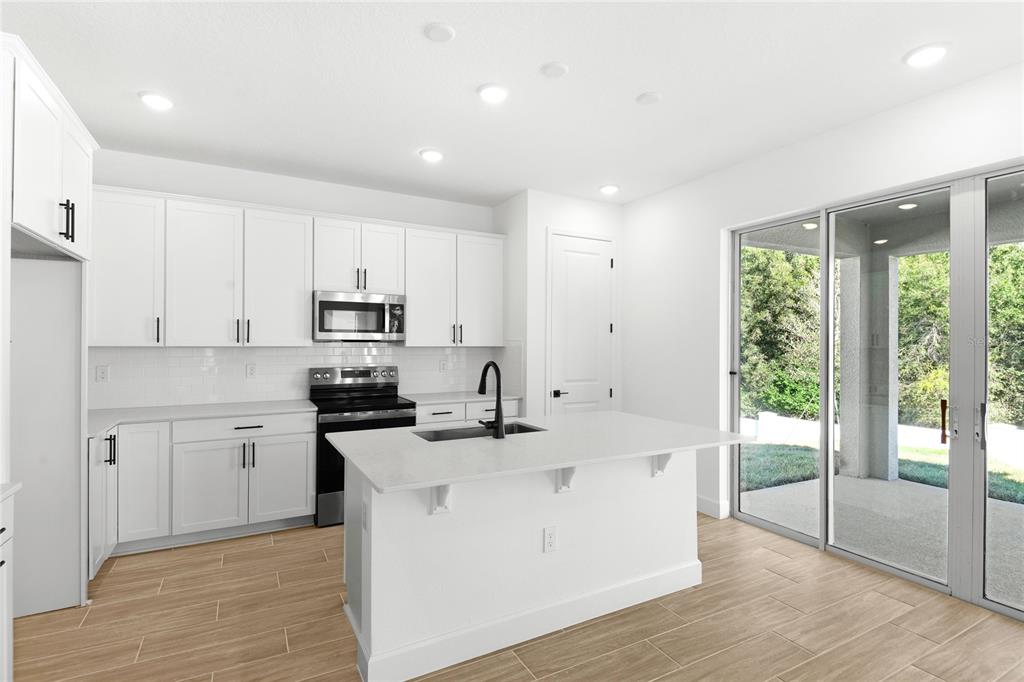 A modern kitchen features white cabinets, stainless steel appliances, a center island, and tile flooring — 740 WEKIVA RIDGE DRIVE, MOUNT DORA, FL