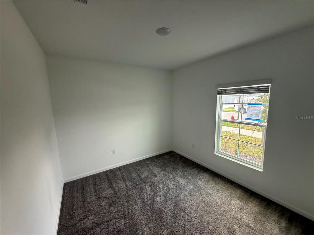 An empty bedroom features white walls, dark gray carpeting, and a single window — 752 TROTTERS DRIVE, EAGLE LAKE, FL
