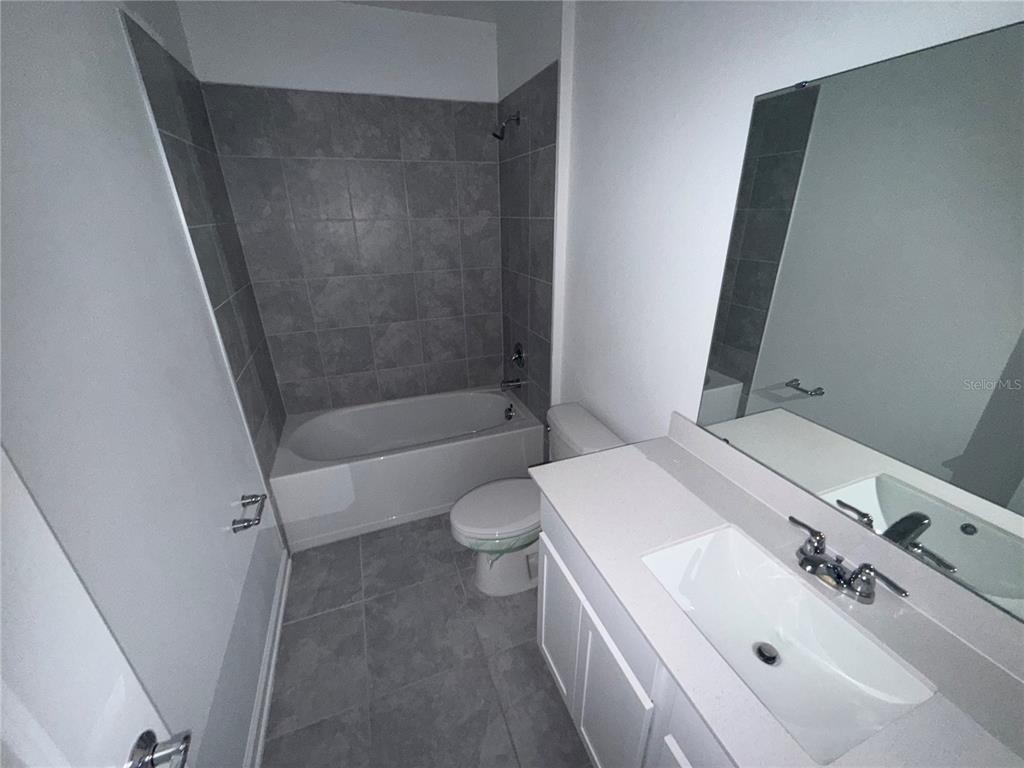 A bathroom features a white vanity, a toilet, and a bathtub with gray tile walls — 752 TROTTERS DRIVE, EAGLE LAKE, FL