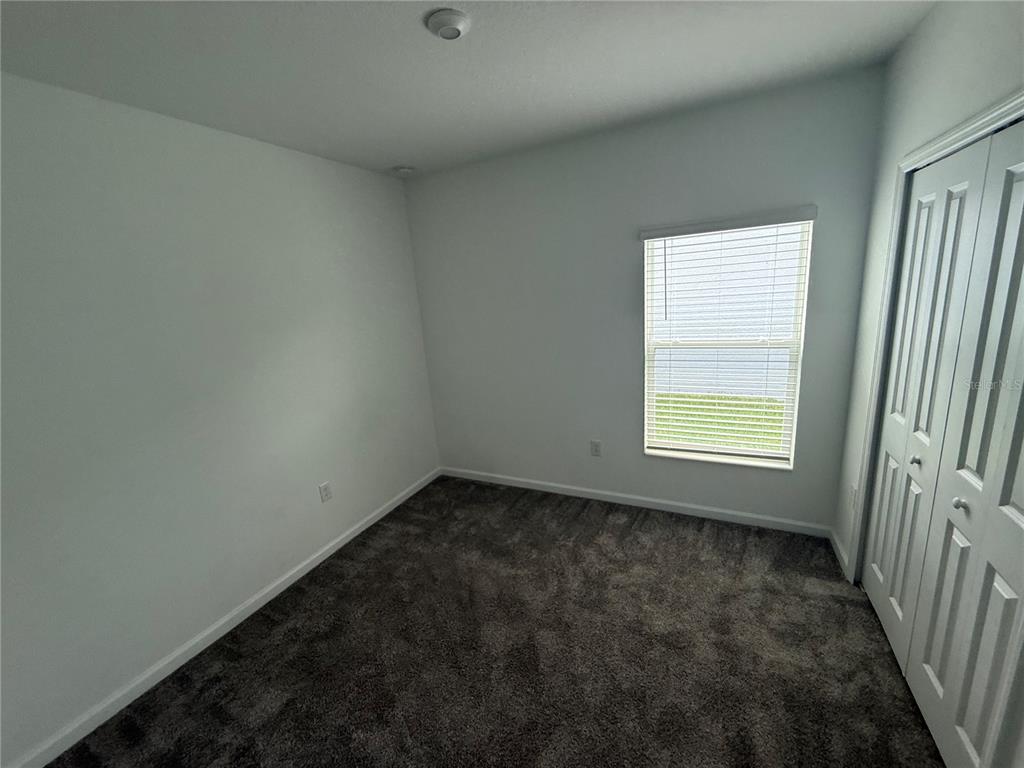 An empty bedroom features gray carpet, white walls, a window with blinds, and a closet — 752 TROTTERS DRIVE, EAGLE LAKE, FL