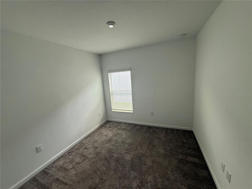 An empty bedroom features gray carpeting, white walls, and a single window with blinds — 752 TROTTERS DRIVE, EAGLE LAKE, FL