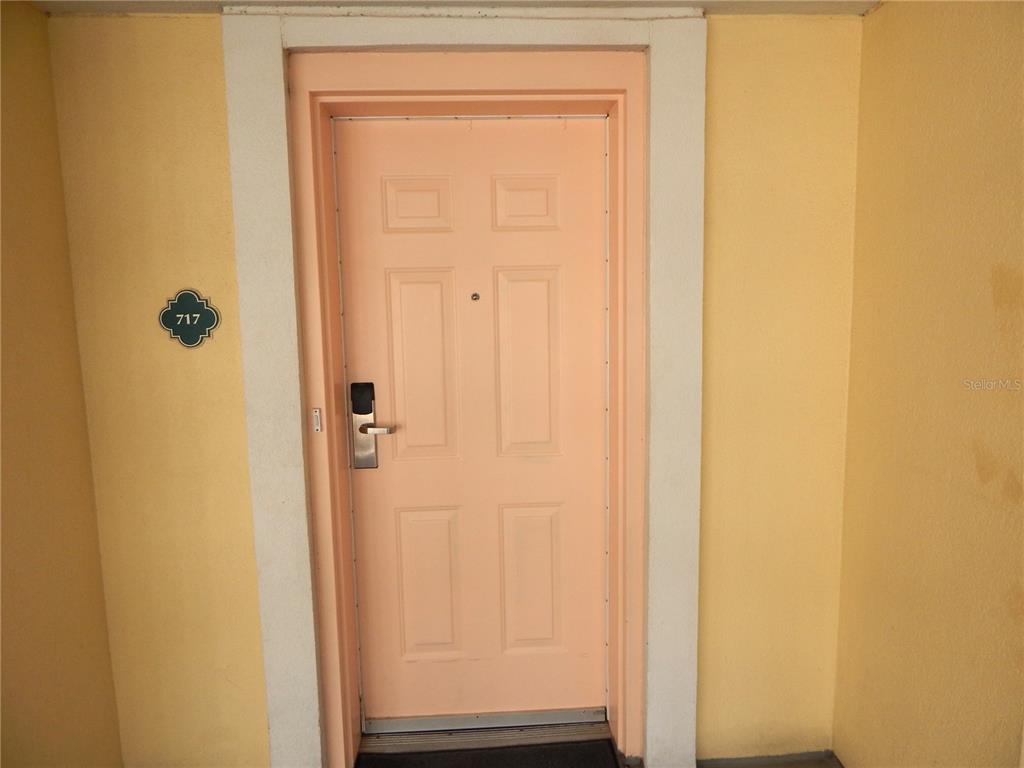 A peach-colored front door with a digital lock is set in a yellow exterior wall — 200 OCEAN CREST DRIVE UNIT 717, PALM COAST, FL