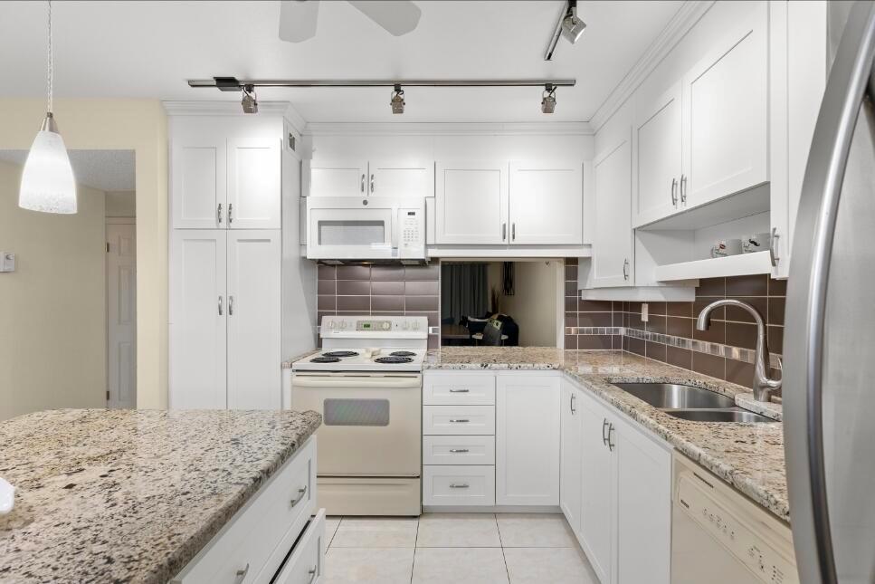A kitchen with white cabinets, granite countertops, stainless steel appliances, and a tile backsplash — 6095 N Sabal Palm Boulevard # 210, Tamarac FL 33319, TAMARAC, FL