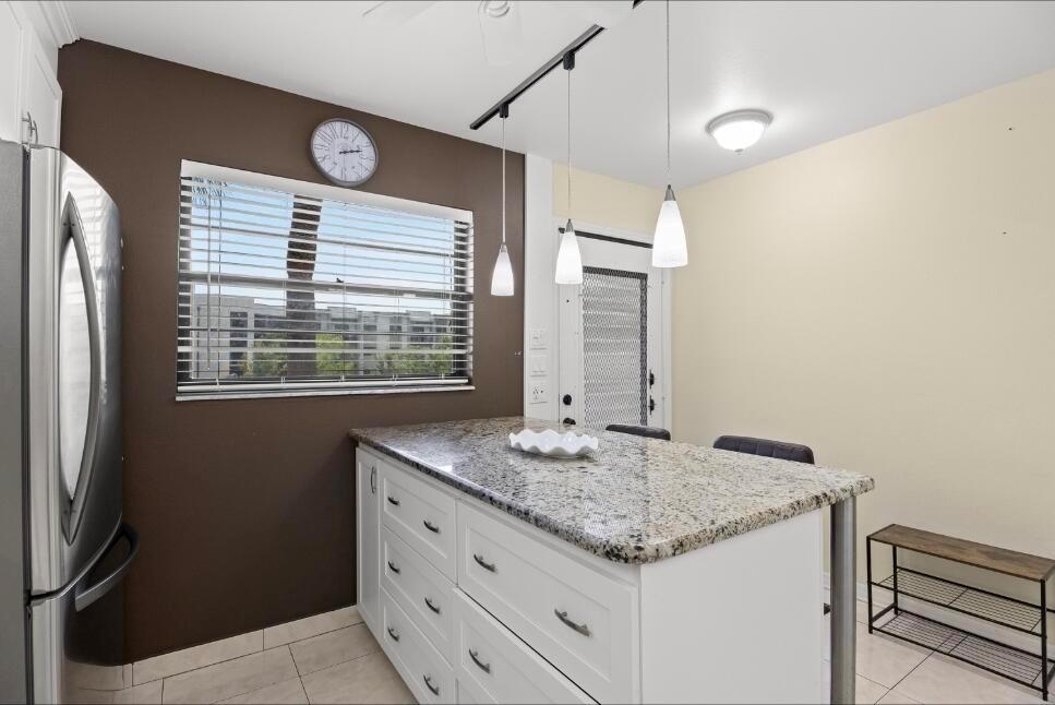 A kitchen features a white island with a granite countertop, dark brown walls, and pendant lighting — 6095 N Sabal Palm Boulevard # 210, Tamarac FL 33319, TAMARAC, FL