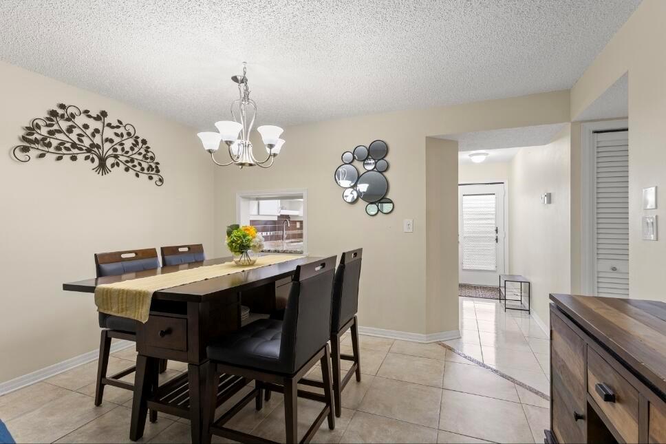 A dining room features a dark wood table, chairs, a chandelier, and tile flooring — 6095 N Sabal Palm Boulevard # 210, Tamarac FL 33319, TAMARAC, FL