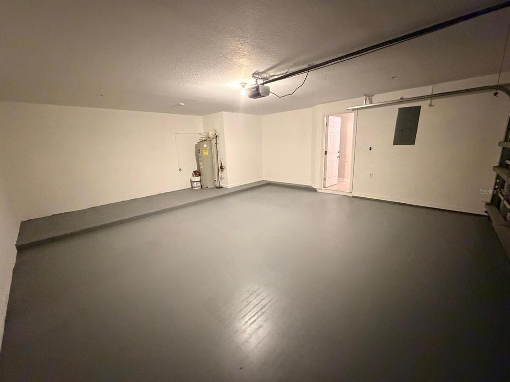 An empty garage with a gray painted floor, white walls, and a water heater — 1807 SHADOW VIEW CIRCLE UNIT 1807, MAITLAND, FL
