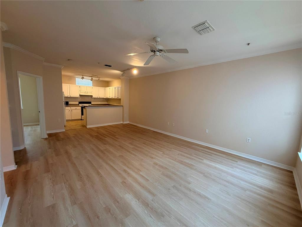 An open-concept living room features light wood-look flooring, a ceiling fan, and a kitchen beyond — 1807 SHADOW VIEW CIRCLE UNIT 1807, MAITLAND, FL