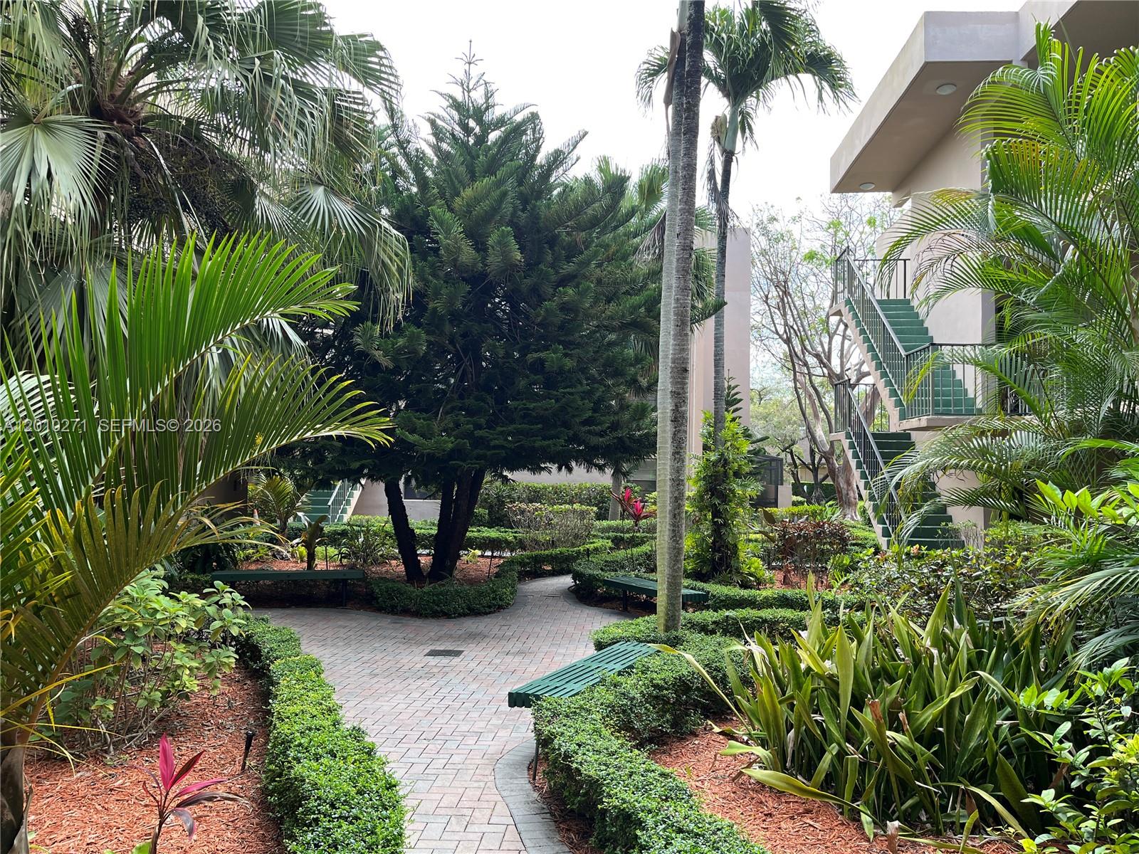 A paved walkway winds through a landscaped courtyard with benches, palm trees, and exterior stairs — 10525 SW 112th Ave # 314, Miami FL 33176, MIAMI, FL
