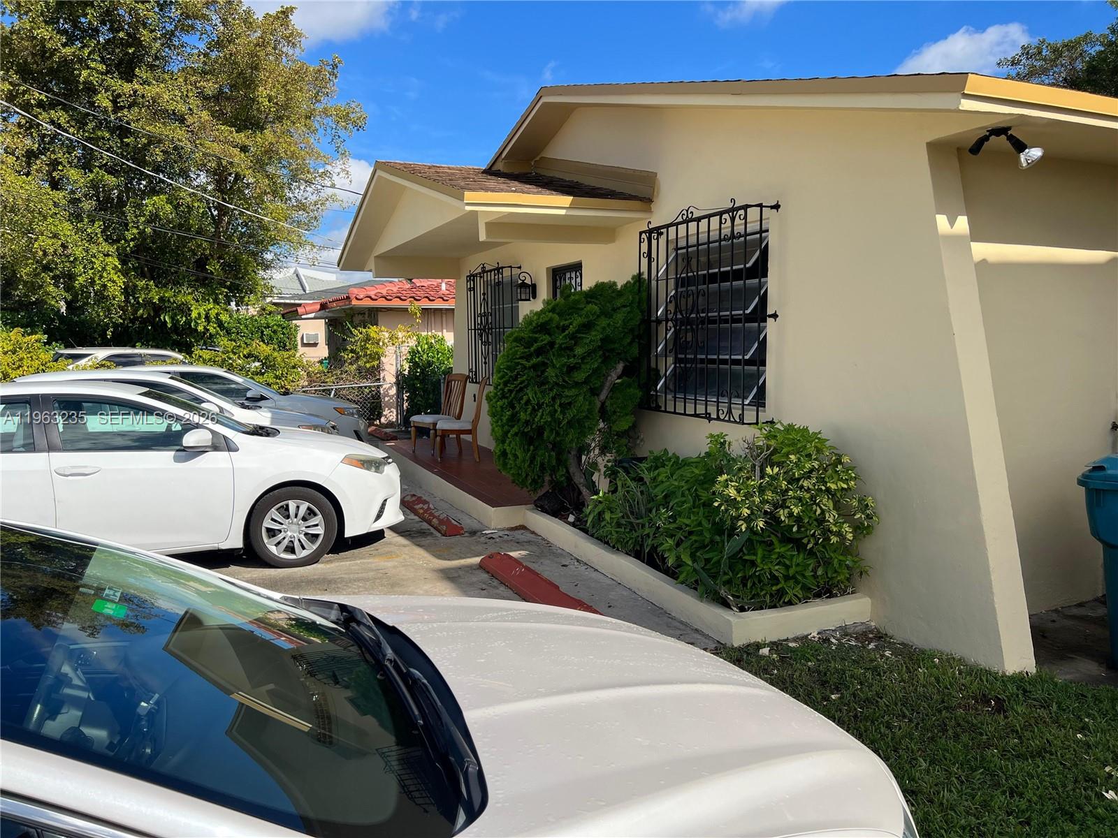 A light-colored house exterior features a small porch, security bars on windows, and parked cars — 733 NW 33rd Ave, Miami FL 33125, MIAMI, FL