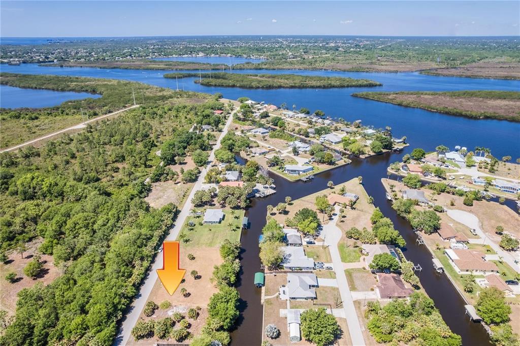 An aerial view shows a vacant, grassy lot marked by an orange arrow near canals — 28426 & 28434 ROYAL PALM DRIVE, PUNTA GORDA, FL