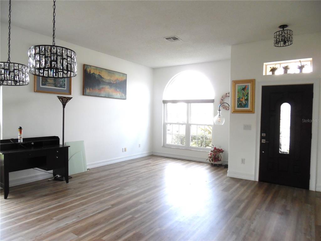 A bright living room features wood-look flooring, a large arched window, and two crystal chandeliers — 16740 GLENBROOK BOULEVARD, CLERMONT, FL
